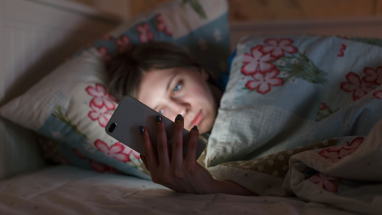 Celular iluminando o rosto de uma pessoa deitada no escuro