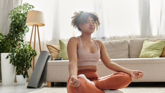 Pessoa meditando sentada no chão com olhos fechados, respirando profundamente.