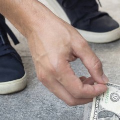 Pessoa encontrando uma nota de dinheiro na rua durante a caminhada