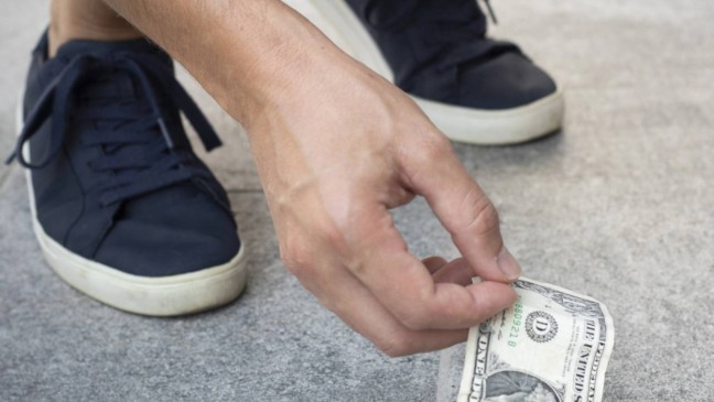 Pessoa encontrando uma nota de dinheiro na rua durante a caminhada