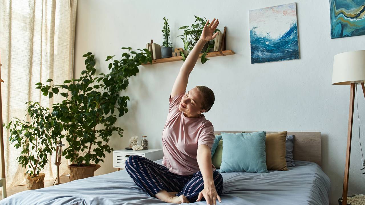 Pessoa fazendo alongamento suave na cama antes de dormir, preparando corpo e mente para descanso.
