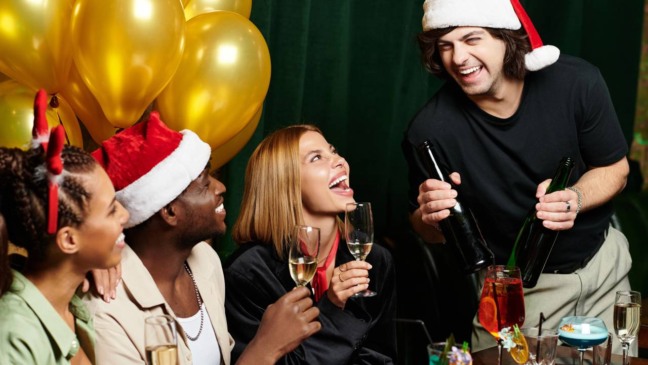 Uma família reunida ao redor da mesa brinca com biscoitos, copos e doces de Natal, rindo enquanto participa de desafios simples e acessíveis que usam materiais comun