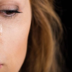 Mulher segurando a cabeça com expressão de dor, sentada em um sofá logo após chorar.