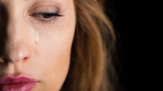 Mulher segurando a cabeça com expressão de dor, sentada em um sofá logo após chorar.