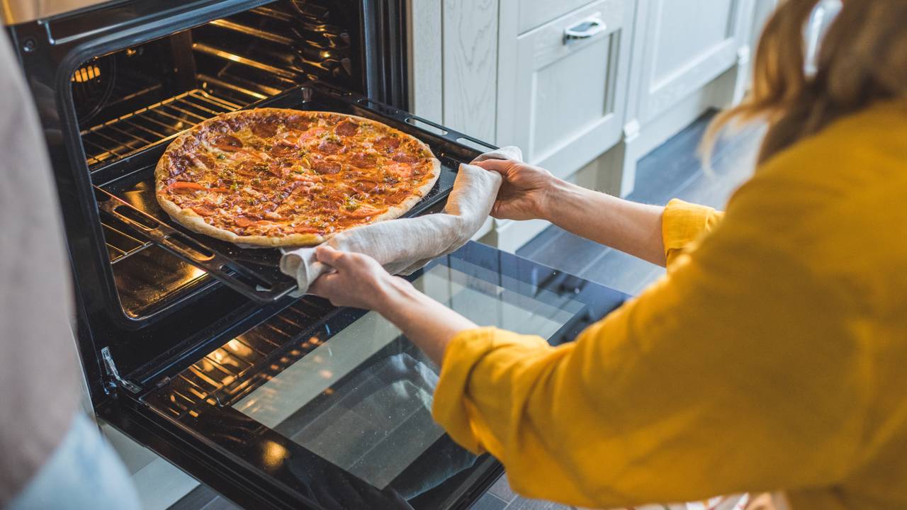 Pessoa colocando a forma com bolo de cenoura no forno preaquecido.
