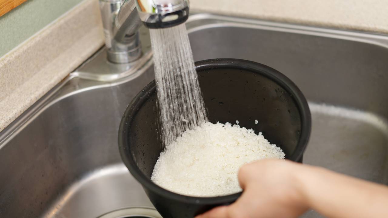 Arroz branco sendo lavado em &aacute;gua corrente para retirar o excesso de amido antes do cozimento.