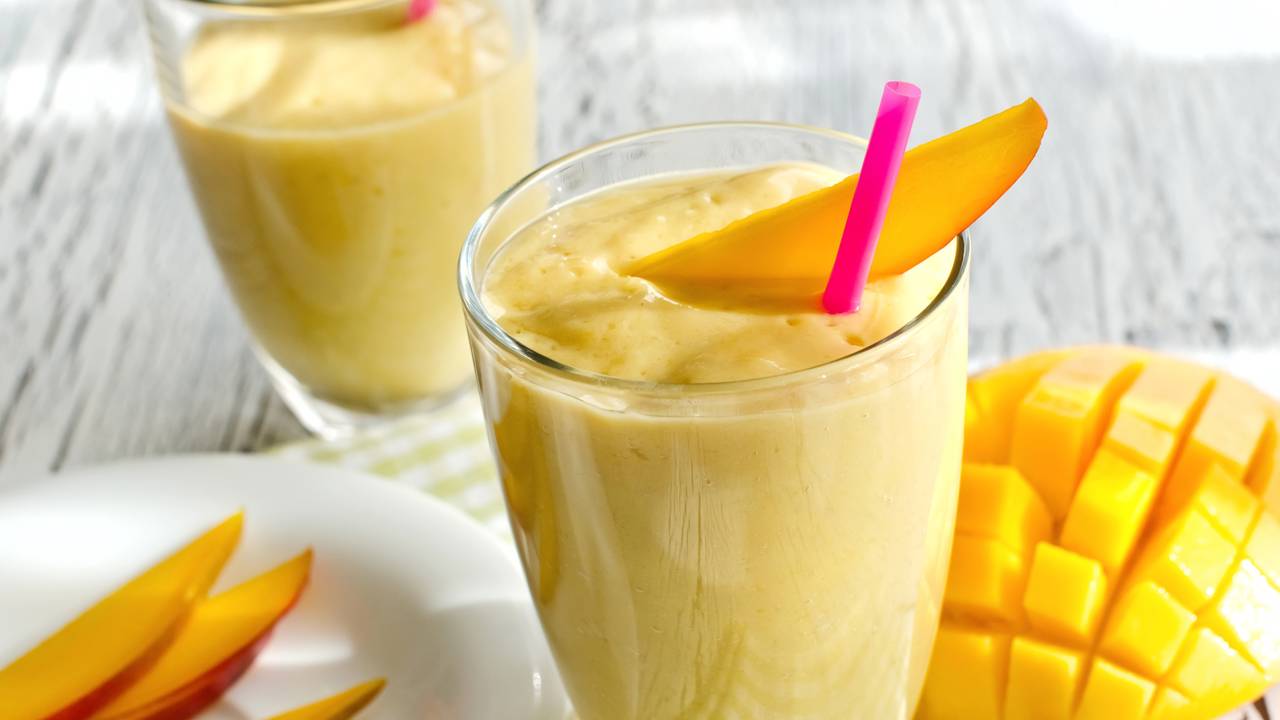 Smoothie tropical gelado feito com manga, abacaxi, &aacute;gua de coco e gelo servido em copo alto
